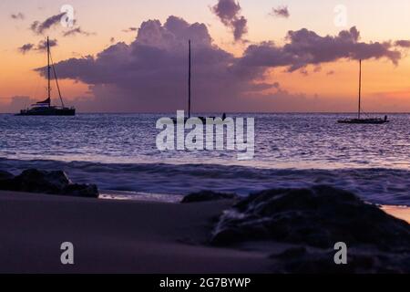 Trois voiliers amarrés dans les Caraïbes au large de la rive près de Frederiksted, Sainte Croix, USVI comme le coucher du soleil se reflète dans les nuages et la mer. Banque D'Images