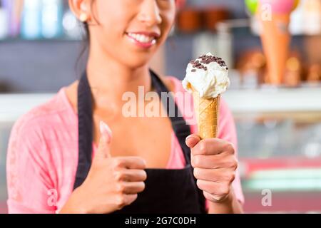 Jeune vendeuse asiatique dans un glacier avec cornet de crème glacée Banque D'Images