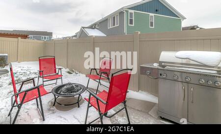 Pano terrasse clôturée de la maison avec barbecue et chaises rouges autour d'un foyer Banque D'Images