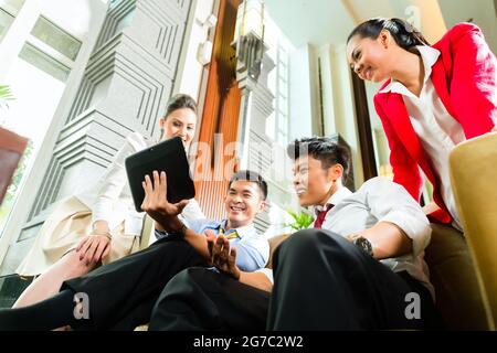 Groupe de quatre affaires Chinois asiatique pour les petites salles de discussion d'équipe dans de luxueux hall de l'hôtel, il y a des documents sur un ordinateur tablette Banque D'Images