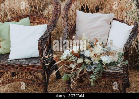 Deux chaises en osier avec coussins et bouquet de fleurs. Chaises en rotin avec des balles de paille en arrière-plan. Style boho Banque D'Images