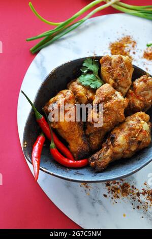 Vue de dessus des ailes de poulet épicées dans un bol avec piment et ingrédients sur fond rouge Banque D'Images