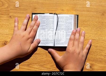 Les mains des enfants tiennent une bible penchée sur une table en bois. Petit livre Sainte Bible.Kid lecture de la sainte bible,closeup.Telsiai,Lituanie.06 04 2021. Banque D'Images