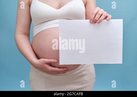 Femme enceinte avec une feuille de papier A4 dans ses mains, fond bleu Banque D'Images