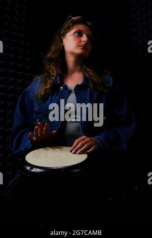 Jouer sur l'instrument ethnique africain de percussion darbuka, photo horizontale. Une jeune femme joue un djembe de tambour assis sur le sol dans un enregistrement Studi Banque D'Images