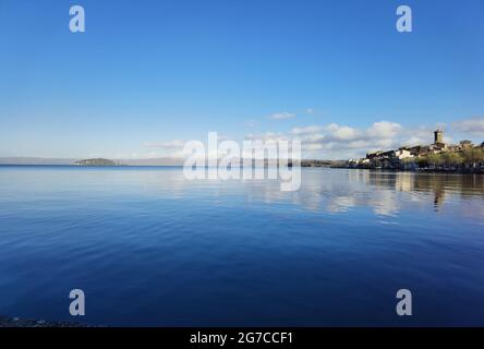 Vue sur le lac Bolsena avec les reflets des maisons et des nuages dans l'eau bleue ondulée par le vent. Banque D'Images