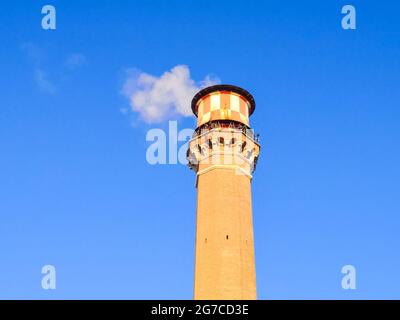 Tour en briques avec une cheminée d'où la fumée blanche sort dans un ciel bleu. Banque D'Images