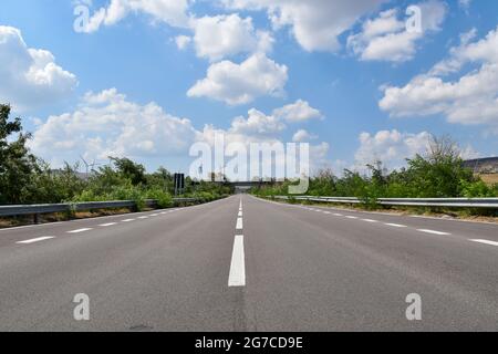 route de banlieue, ou autoroute, vue en perspective sous un ciel bleu avec quelques nuages Banque D'Images