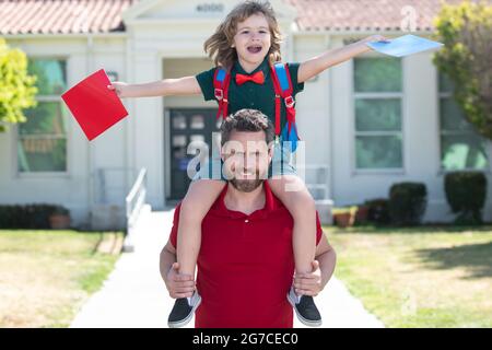 Un père et un fils étonnés courent avec le père après être revenus de l'école. École, famille, éducation et concept de plein air. Papa et fils s'amusent près de l'école Banque D'Images