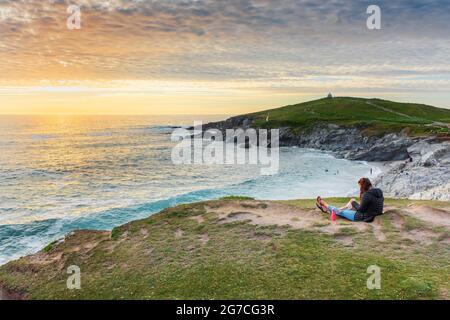 Une femme en vacances assise et profitant du spectaculaire coucher de soleil sur Towan Head et Little Fistral sur la côte de Newquay en Cornouailles. Banque D'Images