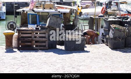 Pesaro, Italie - 09 juillet 2020 : un pêcheur travaille sur son bateau de pêche au port de Pesaro avec les outils du commerce, les filets de pêche et les boîtes Banque D'Images