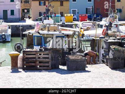 Pesaro, Italie - 09 juillet 2020 : un pêcheur travaille sur son bateau de pêche au port de Pesaro avec les outils du commerce, les filets de pêche et les boîtes Banque D'Images