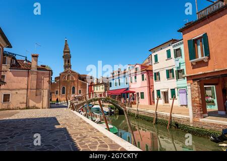 Île de Burano, maisons multicolores, petit canal avec des bateaux amarrés et l'église paroissiale de San Martino Vescovo avec le clocher incliné. Venise. Banque D'Images