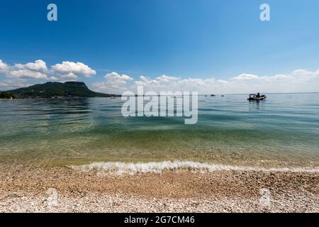 Belle plage sur le lac de Garde (Lago di Garda) en face de la petite ville de Garda. Pointe de San Vigilio (Punta San Vigilio), Vérone, Vénétie, Italie. Banque D'Images