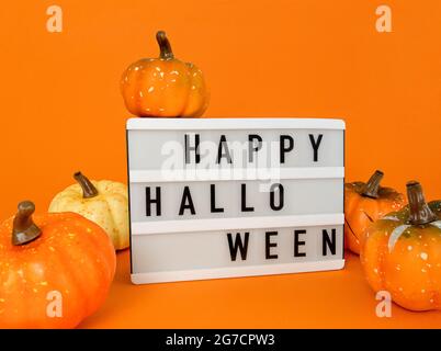 Boîte lumineuse avec une bonne phrase Halloween avec décoration citrouilles sur fond orange. Banque D'Images