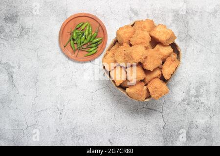 Photo Flat Lay, tahu krispi ou tofu croustillant et piment vert dans un bol de bambou, besek sous marbre abstrait brun Banque D'Images