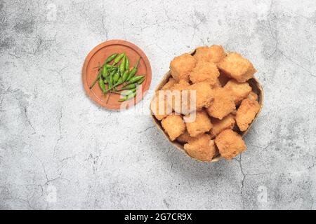 Photo Flat Lay, tahu krispi ou tofu croustillant et piment vert dans un bol de bambou, besek sous marbre abstrait brun Banque D'Images