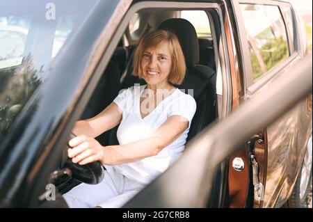 Bonne femme senior conduite assise dans une nouvelle voiture marron, souriant regardant la caméra appréciant voyage.cours de conduite et concept d'assurance vie. Concept de l'activité des retraités Banque D'Images