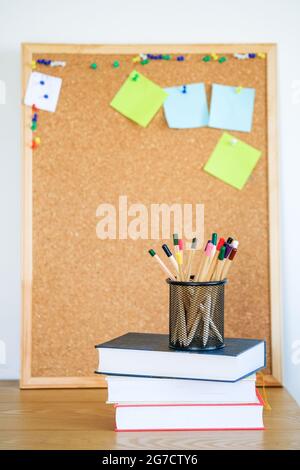 Une pile de livres, de lunettes, de nombreux crayons dans le support en métal sur fond de bois de liège. Le concept de l'éducation. Copier espace vide.modèle. Banque D'Images