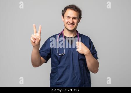 Beau jeune homme portant un médecin stéthoscope sur fond blanc isolé avec sourire heureux face à l'appareil photo faisant un clin la victoire. Nombre Banque D'Images