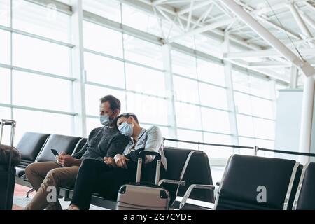 Homme et femme avec masques de visage assis à l'aire d'attente de l'aéroport. Couple à l'aéroport pendant le confinement du virus Corona. Banque D'Images