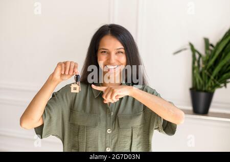 Concept de relocalisation. Photo de la femme indienne excitée qui se déplace dans une nouvelle maison ou un nouvel appartement. Joyeuse femme de course mixte regardant l'appareil photo et pointe le doigt sur les clés avec le porte-clés dans sa main Banque D'Images