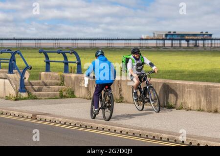 Southport, Merseyside. Météo Royaume-Uni. 13 juillet 2021 : les premiers rayons du soleil et le réchauffement des températures atteignent 20 °C, les résidents locaux faisant de légers exercices sur la promenade du front de mer de la station. Les activités sur la route côtière comme l'habitat des dunes et le gazage des sables (accrétion), semblent s'étendre sur la côte de Fylde. La côte de Sefton a du mal à repousser deux envahisseurs : la mer et les herbes dures qui se déferle sur la plage, ce qui finira par entraîner la jetée au fur et à mesure que se forment les dunes de sable. Crédit; MediaWorldImages/AlamyLiveNews Banque D'Images