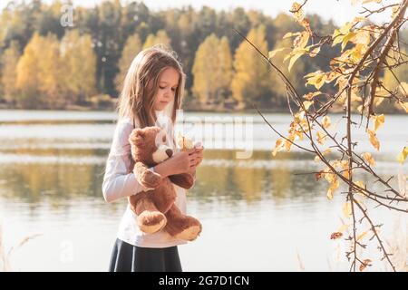 Une fille avec un ours en peluche tient une feuille sèche sur le bord de la rivière en forêt Banque D'Images