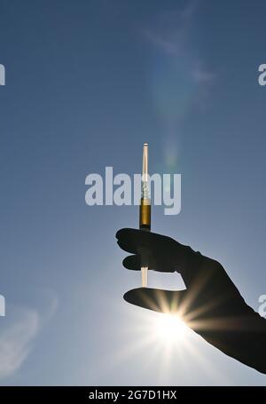 seringue avec injection dans une main bleue contre le fond du ciel Banque D'Images