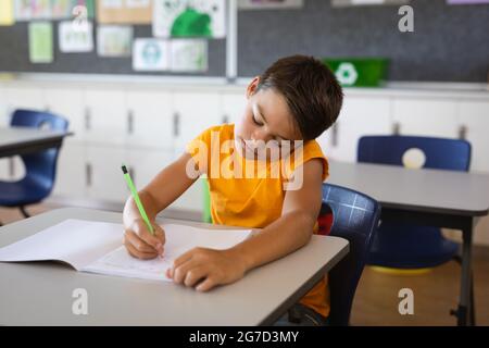 Garçon caucasien étudiant en étant assis sur son bureau dans la classe à l'école Banque D'Images