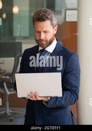 un homme d'affaires mature et concentré travaille en ligne sur un ordinateur moderne en dehors du bureau, une entreprise agile. Banque D'Images