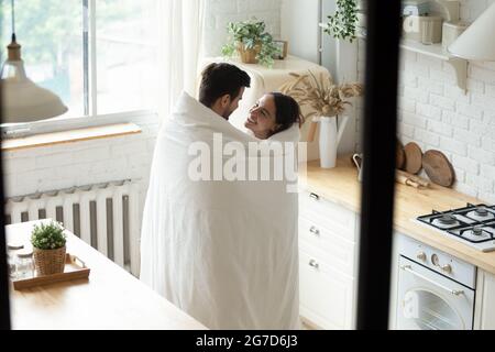 Couple aimant debout dans la cuisine moderne enveloppé ensemble dans une couverture Banque D'Images