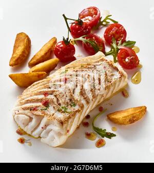 Composition à grand angle de délicieux poissons de pollack cuits au four et de tomates cerises disposés sur une surface blanche avec de savoureuses quartiers de pommes de terre Banque D'Images