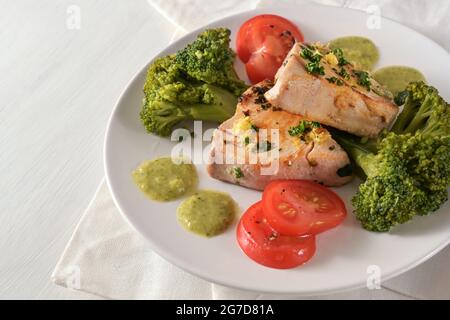 Repas sain avec filet de thon frit, brocoli, tomates, persil et sauce citron vert sur une assiette blanche et une table légère, espace de copie, foyer sélectionné, Banque D'Images