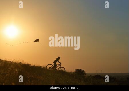 Silhouette Young Boy jouant avec son Kite Riding sur vélo Banque D'Images
