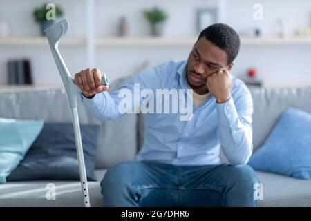 Malheureux Afro-américain gars penchée sur la béquille, souffrant de la dépression après une blessure à la maison, foyer sélectif Banque D'Images