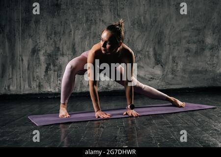 Musculeux jeune femme sportive avec corps parfait beau porter vêtements de sport étirement du corps et faire des exercices de fente latérale sur le tapis de yoga. Banque D'Images