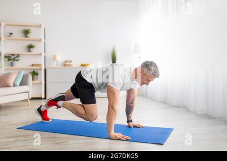 Sportif homme mature faisant de la planche de course entraînement sur tapis de sport dans le salon à la maison, espace libre Banque D'Images