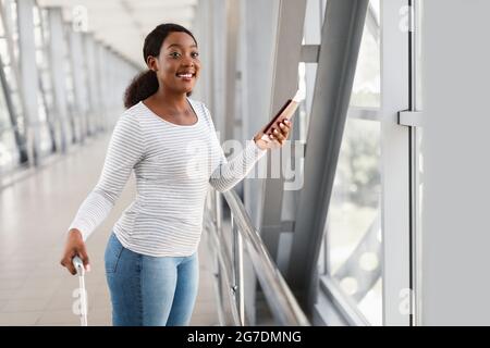 Heureuse femme noire excitée voyageant, regardant par la fenêtre à l'aéroport Banque D'Images