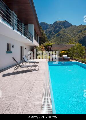 Maison moderne de deux étages avec grande piscine donnant sur les montagnes. Deux chaises longues pour profiter du soleil, deux chaises longues et un grand parasol Banque D'Images