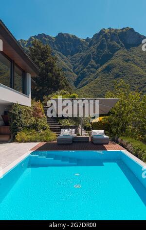 Maison moderne de deux étages avec grande piscine donnant sur les montagnes. Deux chaises longues et un grand parapluie ouvert pour profiter de vos vacances. Personne à l'intérieur Banque D'Images