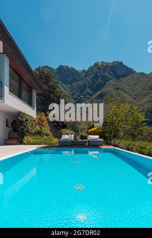 Maison moderne de deux étages avec grande piscine donnant sur les montagnes. Deux chaises longues et un grand parapluie ouvert pour profiter de vos vacances. Personne à l'intérieur Banque D'Images