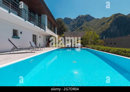 Maison moderne de deux étages avec grande piscine donnant sur les montagnes. Deux chaises longues pour profiter du soleil, deux chaises longues et un grand parasol Banque D'Images