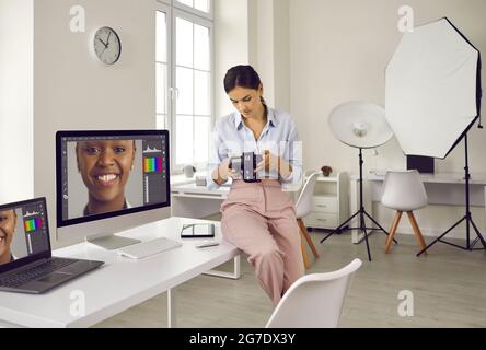 Photographe regardant des photos sur son appareil photo tout en étant assis sur son bureau avec ses ordinateurs Banque D'Images