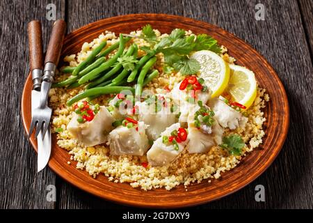 Bacalhau com todos, morue au bulgur, haricots verts à la vapeur, saupoudrées de piments forts et d'oignons verts sur une assiette rustique, sur une table en bois sombre Banque D'Images