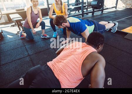 Deux hommes ont une compétition de poussée dans la salle de gym avec les filles les encourageant Banque D'Images