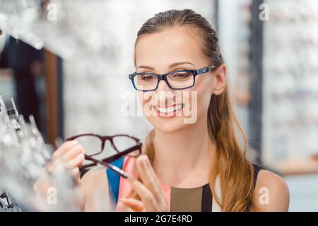 Femme étant satisfaite des nouvelles lunettes qu'elle a achetées dans le magasin les tenant devant son visage Banque D'Images