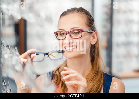 Femme étant satisfaite des nouvelles lunettes qu'elle a achetées dans le magasin les tenant devant son visage Banque D'Images