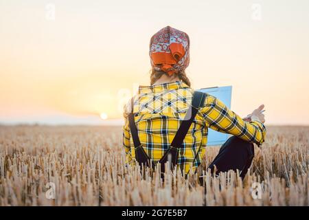 Agriculteur femme calculant le rendement de récolte après une longue journée d'utilisation stylo et papier Banque D'Images