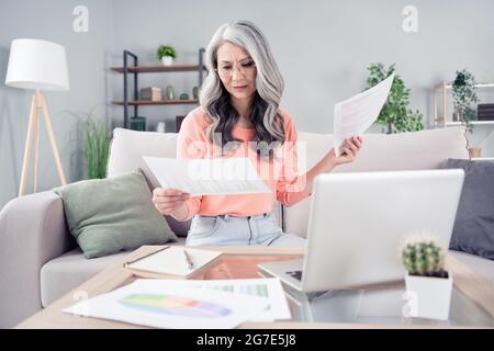 Portrait d'une femme élégante et attirante assise sur un canapé avec un ordinateur portable pour lire des documents à la maison à l'intérieur Banque D'Images